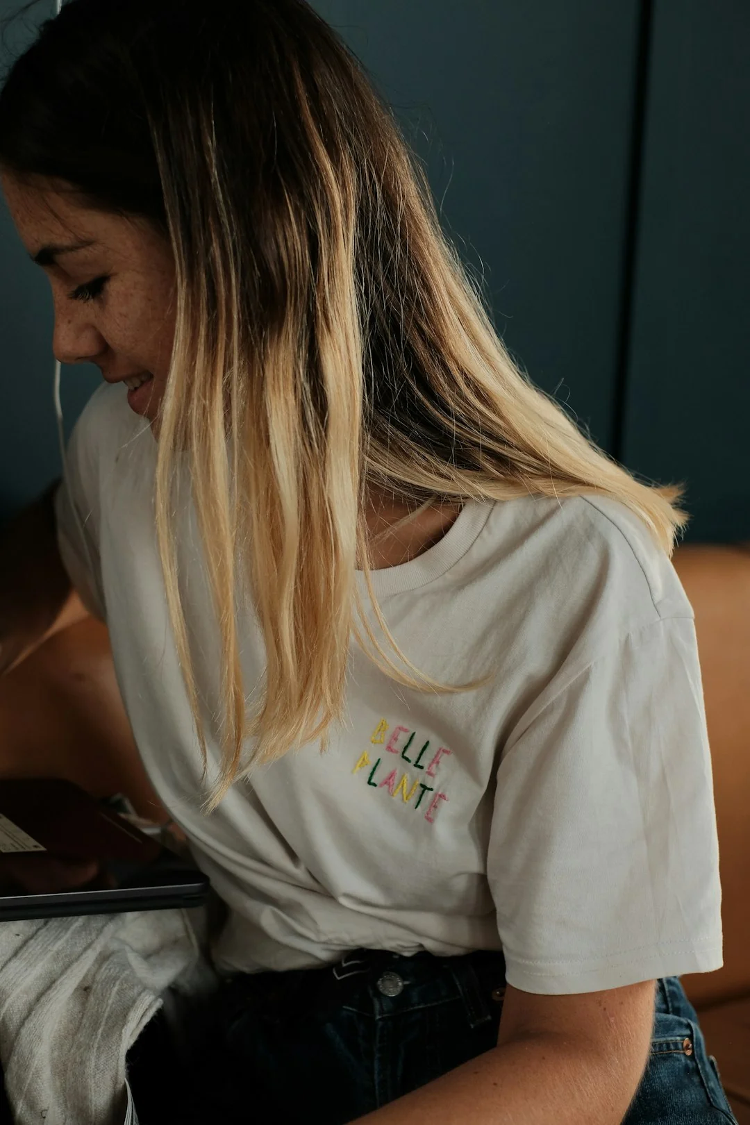 Main tenant un smartphone affichant l’interface d’une application de portefeuille numérique, avec un écran d’ordinateur flou en arrière-plan.